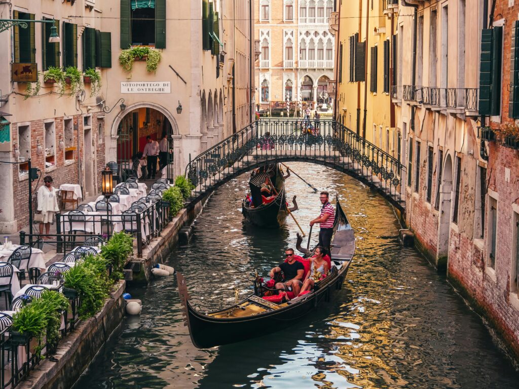 Charming scene of gondolas navigating a canal in Venice, Italy with a backdrop of historic buildings and a pedestrian bridge.